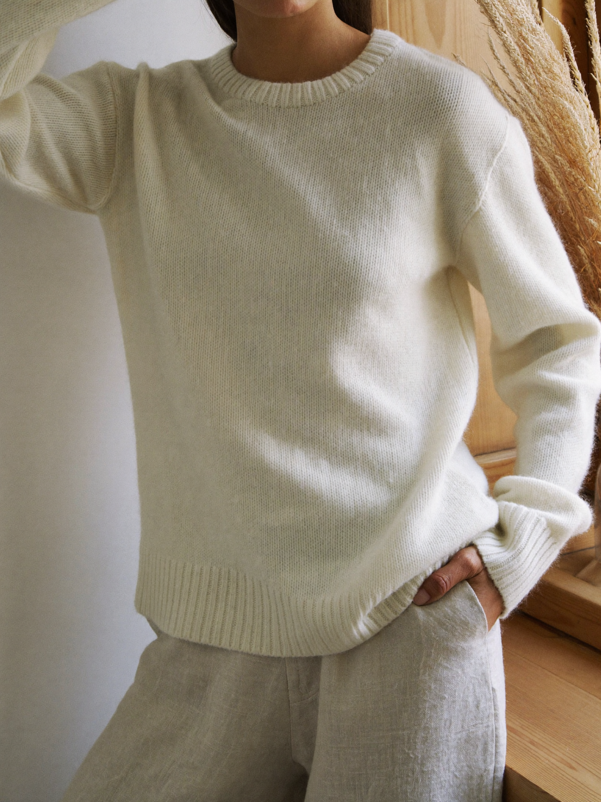 Cream knit sweater and linen trousers by a sunlit window
